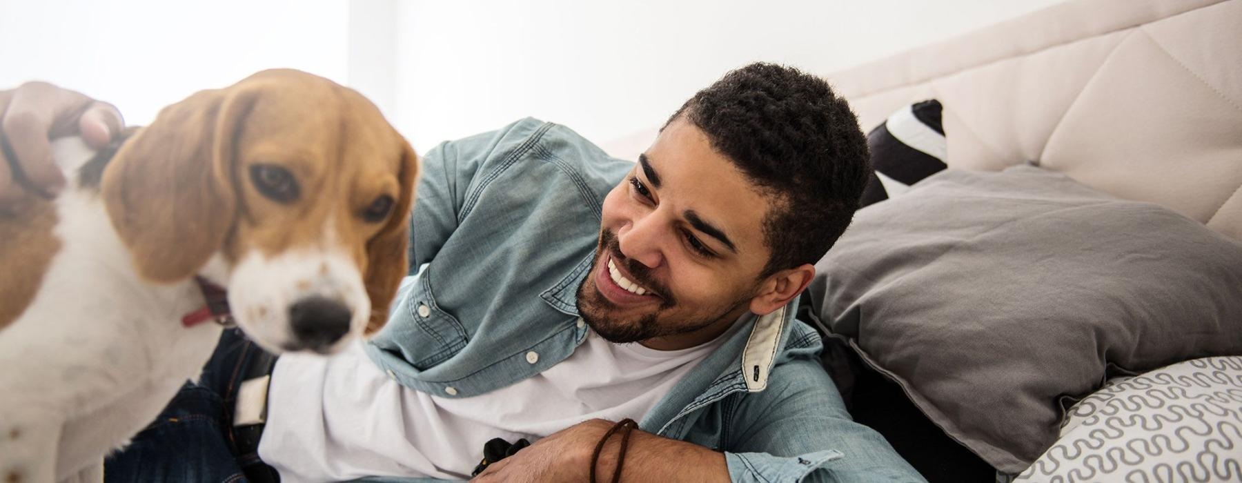 man smiles and pets his dog on a bed